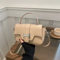Minimalist beige leather crossbody bag with silver buckle held by hand in a chic setting - Khaki