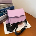Lavender small square crossbody bag with wide black strap on wooden desk background - Pink