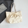 Cream tote bag with large bow decoration and slim shoulder straps on grey background - White