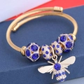 Detail of gold twisted bangle featuring a crystal bee charm and blue beads on a stand - Blue