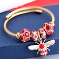 Macro view of a gold twisted wire bracelet featuring a detailed crystal bee charm - Red