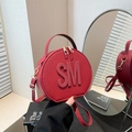 Elegante bolso redondo rojo con letras en relieve y correa dorada en un estudio de diseño - Rojo