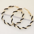 Close-up of golden twisted hoop earrings featuring black bead embellishments and texture - Black