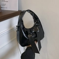 Glossy black handbag with large bow accent and silver chain strap in elegant indoor setting - Black
