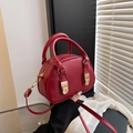 Detail of red shell handbag with gold hardware and adjustable strap held by model - Red