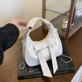 White hobo shoulder bag with a large bow detail and silver chain on a book background - White