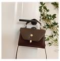 Detail of a dark brown trapezoid crossbody bag with gold metal hardware on a door handle - Brown