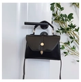 Detail of black leather crossbody bag with golden 'C' buckle hanging on a white door - Black