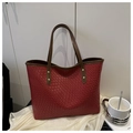 Close-up of red woven leather tote bag texture with brown handles and gold rivets - Red