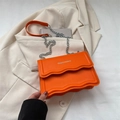 Bolso bandolera naranja brillante con solapa ondulada y cadena de plata sobre blazer - Naranja