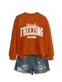 Detailed flat lay of orange 'literally freezing' sweatshirt and ripped denim shorts set - S / Tops / Burnt Orange (White Print)