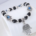 Detailopname van Hamsa Hand en Evil Eye bedels aan een zwarte kralenarmband voor dames - Zwart