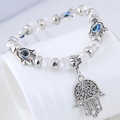 Detailopname van kristallen Hamsa Hand armband met blauwe Evil Eye bedels op een standaard - Wit