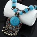Dettaglio di collana boho con pietre turchesi, campanelli in bronzo e frange su supporto bianco - Collana Blu