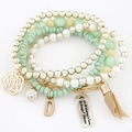 Detail of layered beaded bracelet with mint green beads, flower charms and beige tassel - Green