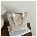 Detalle de bolso tote de pana beige claro con etiqueta bordada en mesa de madera - Caqui