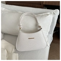 Detail of white woven texture handbag with golden hardware on soft white pillow - White
