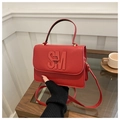 Detail der roten Handtasche mit Litschi-Struktur und SM-Metallschnalle auf einem Kaffeetisch - Rot