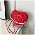 Macro detail of red heart-shaped quilted bag with pearl accents and silver bow - Red