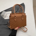 Détail d'un sac à main en cuir marron vintage avec imprimé monogramme M sur veste grise - Marron