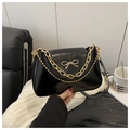 Detailed shot of a black glossy shoulder bag featuring a gold bow and metallic chains - Black