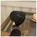 Detalle del bolso negro acolchado con forma de corazón y cadena en una cafetería - Negro