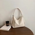 Creamy white hobo bag with front zipper pocket on a wooden desk with a black cup - Off White