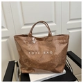 Detail of waterproof brown PVC tote bag with white TOTE BAG text on a black chair - Brown