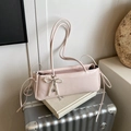 Elegant pink underarm bag with pearl bow charm placed on a vintage book and suitcase. - With Pearl Bow Pendant Style / Pink