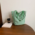 Green and white striped canvas tote bag with metal logo on a vintage wooden table - Green Side A (Striped)
