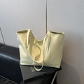 Bolso tote amarillo claro minimalista con correas ajustables sobre un sofá oscuro - Amarillo