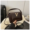 Detailed close-up of dark brown patent leather handbag with golden V-shaped metal logo - Brown
