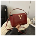 Close-up of glossy wine red patent leather handbag with a gold V-shaped buckle detail - Red