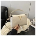 Detail of elegant cream faux leather handbag with golden V-shaped buckle on white fabric - White