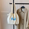 Close-up of off-white canvas tote bag with blue Beach lettering hanging on a rack - Off White