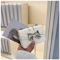 Nahaufnahme einer weißen Mini-Leder-Tasche mit silberner Metallschleife und Kette - Gebrochenes Weiß