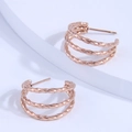 Elegante roségouden triple twisted creolen op een wit geometrisch voetstuk - Roségoud
