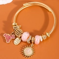 Goldenes Seilarmband mit rosa Kristallanhängern und Sonnenperle auf braunem Hintergrund - Rosa