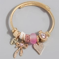 Dettaglio del bracciale dorato con ciondoli a cuore rosa, fiocco e incisione LOVE - Rosa