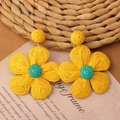 Detail of bohemian yellow and blue raffia flower earrings on a vintage paper background - Yellow