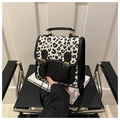 Close-up of leopard print flap detail and gold buckles on a black leather handbag - Black