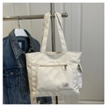 Dettaglio borsa tote in tela bianca con tasca frontale a zip e stemma decorativo Good Luck - Bianco