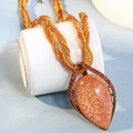 Detail einer böhmischen orangefarbenen Perlenkette mit Tropfenanhänger auf weißer Tasse - Orange