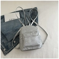 Detalle de mochila plateada metalizada con bolsillo frontal y correas finas sobre denim - Plateado