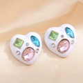 Macro detail of heart-shaped earrings with colorful crystals on satin background - White