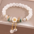 Elegant beaded bracelet with floral charms and crystals on a soft display base - White