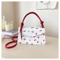 Detail of white leather shoulder bag with red cherry prints and red handle on a desk - Red