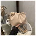 Detalle de bolso saco plisado beige con logo dorado y colgante de peluche en la mesa - Con Colgante / Caqui