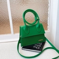 Vibrant green trapezoid handbag with gold logo and circular top handle in a minimalist style - Green