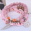 Nahaufnahme eines mehrlagigen Perlenarmbands mit Eiffelturm-Anhänger und Flügel-Detail - Rosa